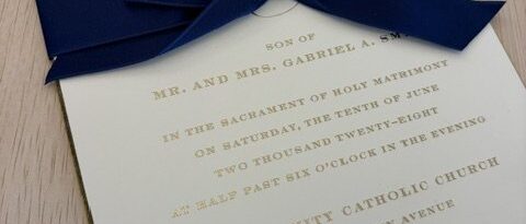 Gold foil wedding invitation tied with a navy velvet ribbon